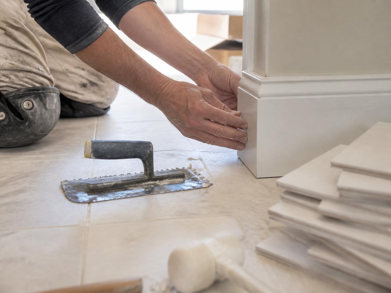 Craftsman installing tile and baseboard trim in a renovated room